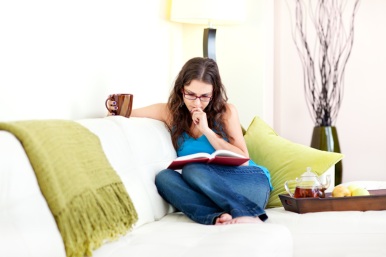 Young woman reading book drinking tea on comfortable couch at home